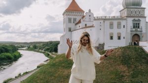 A joyful woman dances in front of a historical castle by a peaceful river.