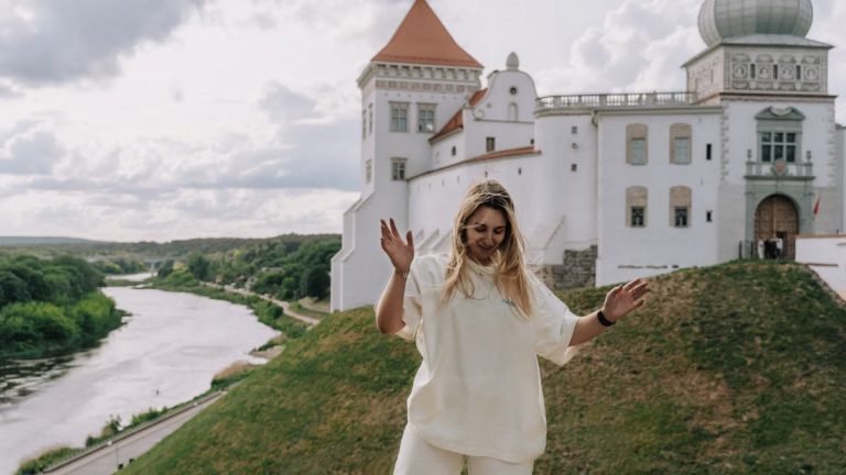 A joyful woman dances in front of a historical castle by a peaceful river.